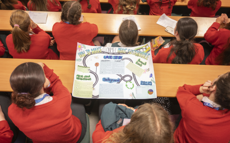 An image of students in a lecture hall with a poster on a table
